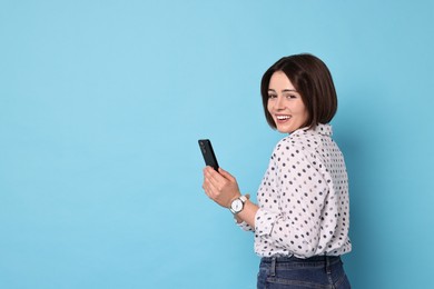 Smiling woman with smartphone on light blue background. Space for text