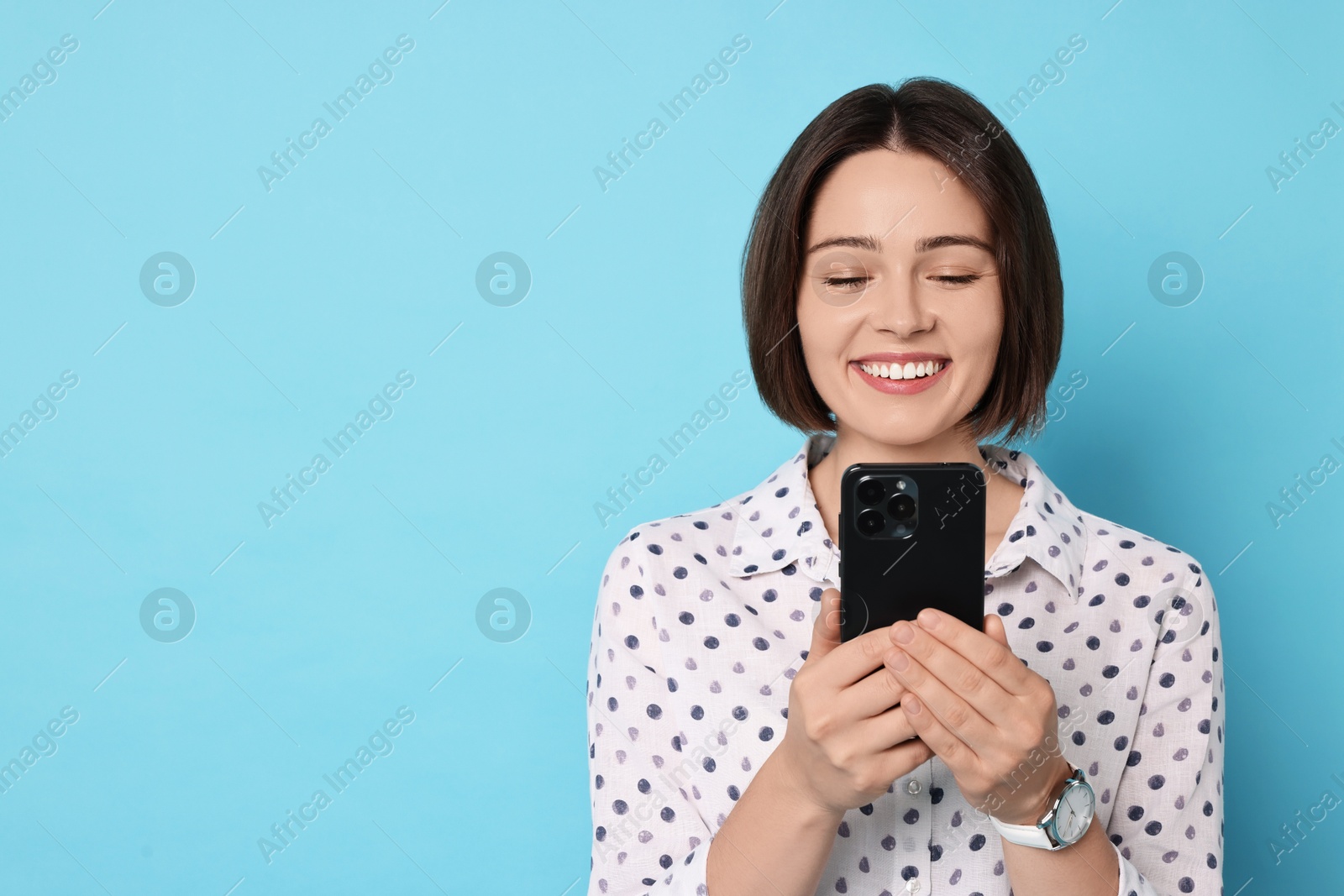 Photo of Smiling woman with smartphone on light blue background. Space for text