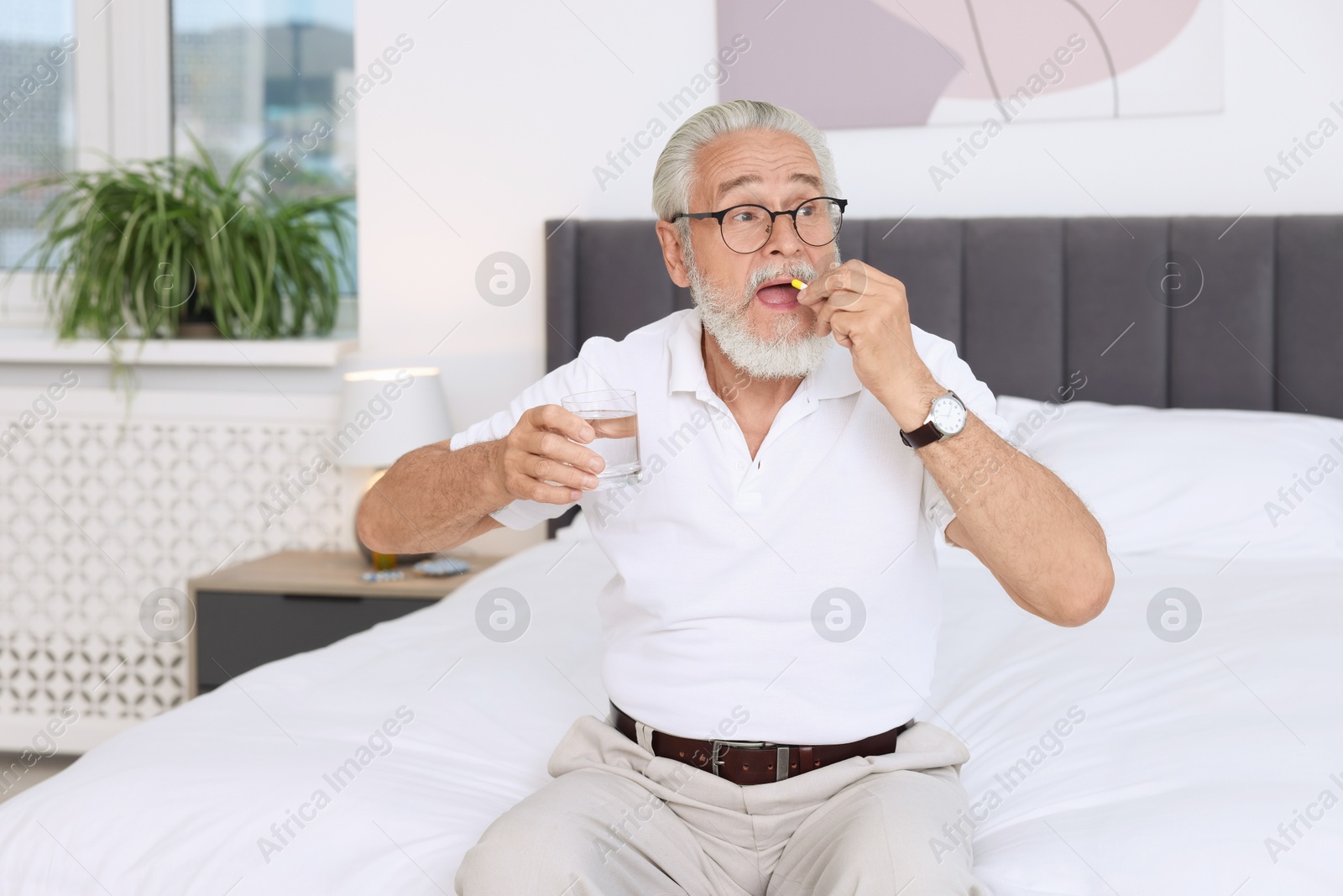 Photo of Senior man with glass of water taking pill at home