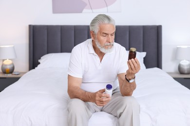 Photo of Senior man with bottles of pills on bed indoors