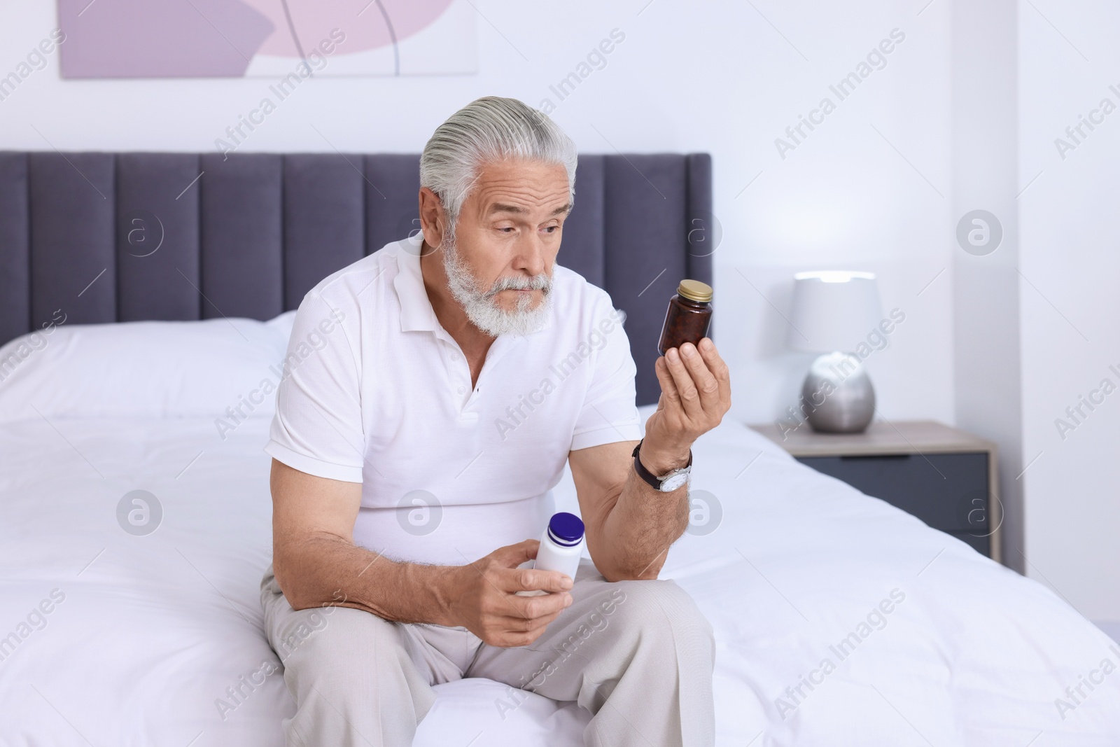 Photo of Senior man with bottles of pills on bed indoors