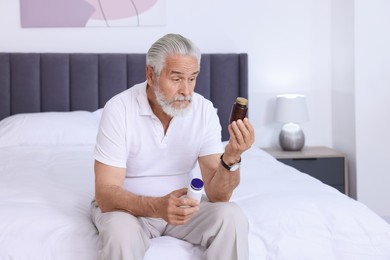 Senior man with bottles of pills on bed indoors