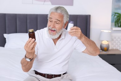 Senior man with bottles of pills on bed indoors