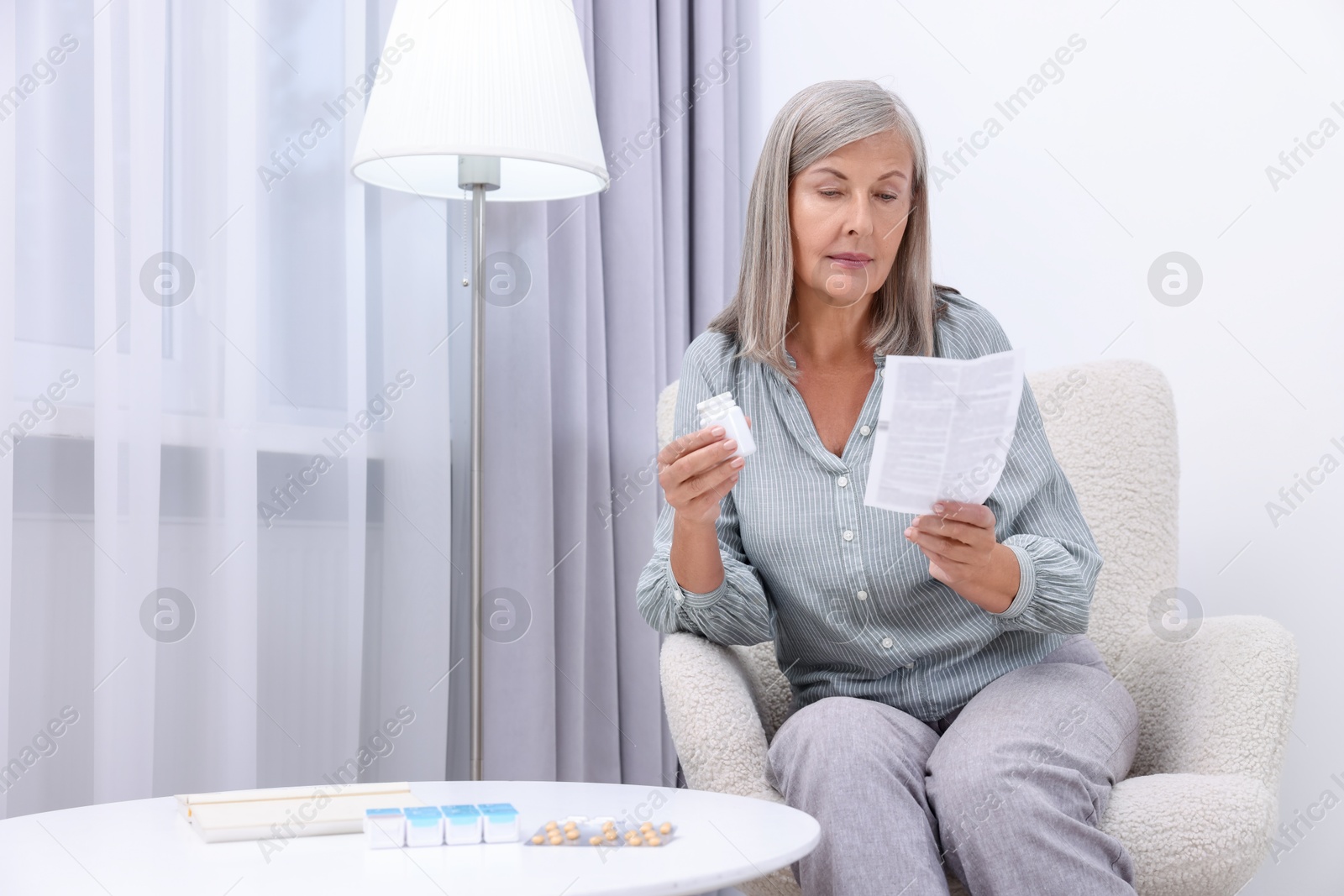 Photo of Senior woman with bottle of pills reading medicine instruction in armchair at home