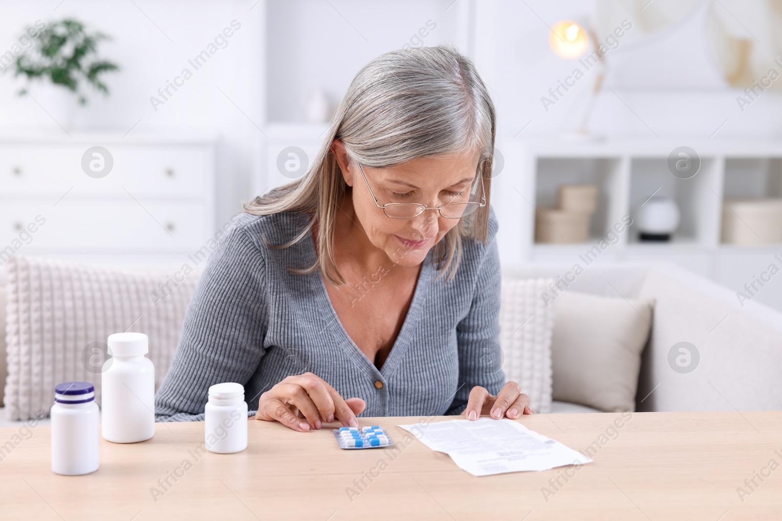 Photo of Senior woman reading medicine instruction at table indoors