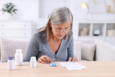 Senior woman reading medicine instruction at table indoors