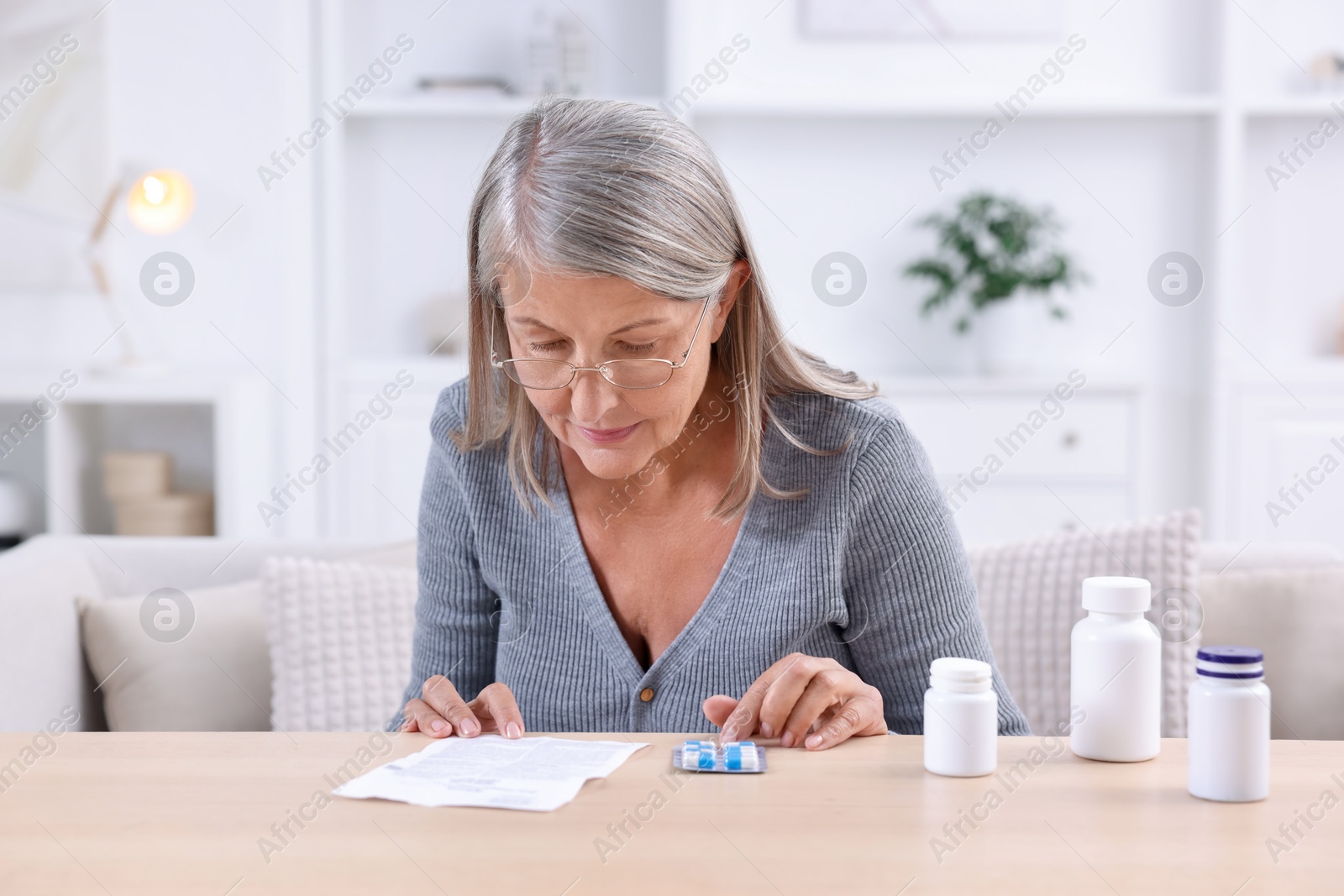 Photo of Senior woman reading medicine instruction at table indoors