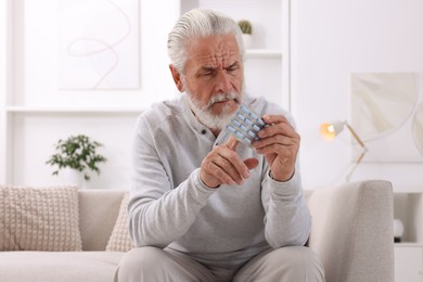 Senior man holding blister with pills at home