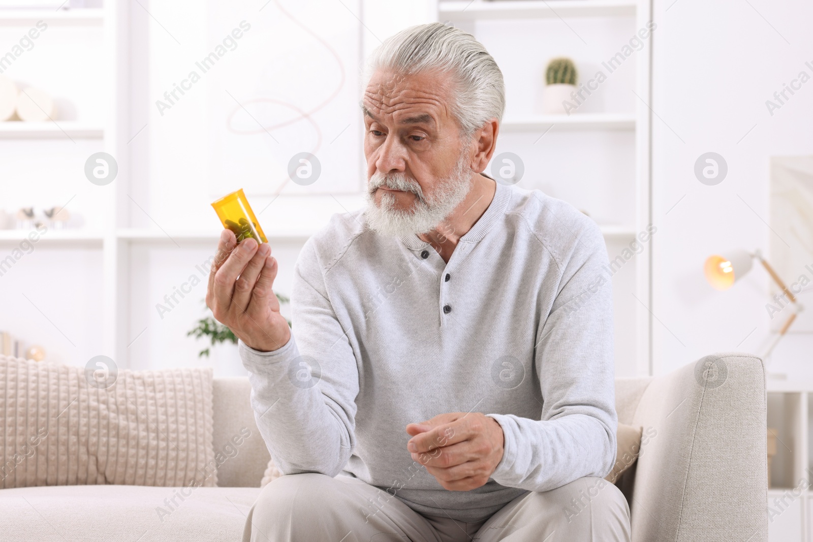 Photo of Senior man holding bottle with pills at home