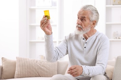 Photo of Senior man holding bottle with pills at home