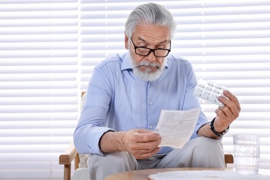 Senior man with pills reading medicine instruction at home