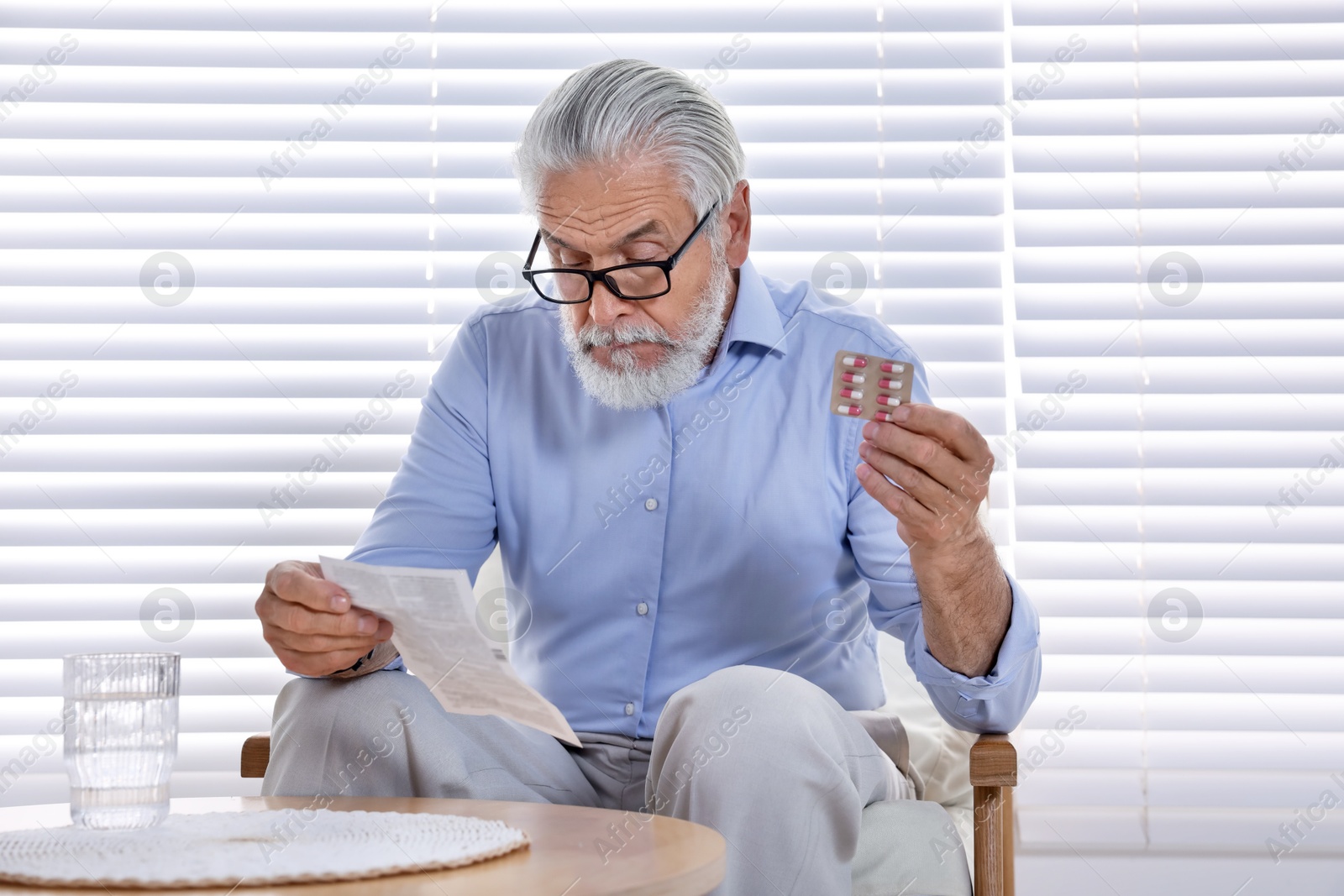 Photo of Senior man with pills reading medicine instruction at home