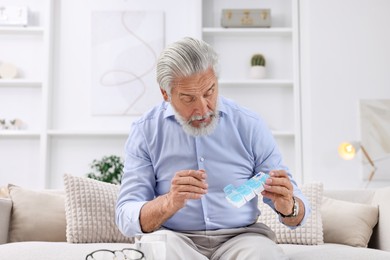 Senior man with pill organizer on sofa at home