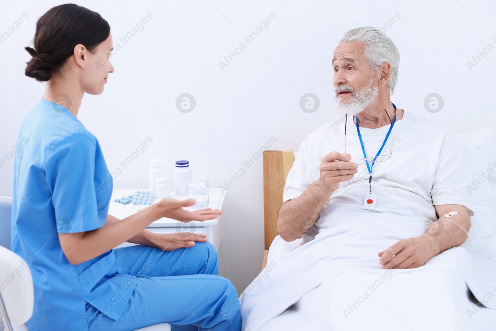 Photo of Senior man with emergency call button talking to nurse in hospital