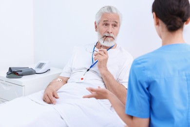 Photo of Senior man with emergency call button talking to nurse in hospital