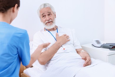 Photo of Senior man with emergency call button talking to nurse in hospital