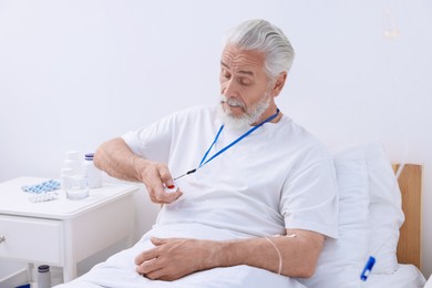 Senior man pressing emergency call button on bed in hospital