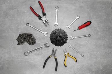 Photo of Wrenches, pliers, bicycle tire, cassette and chain on grey textured background, flat lay