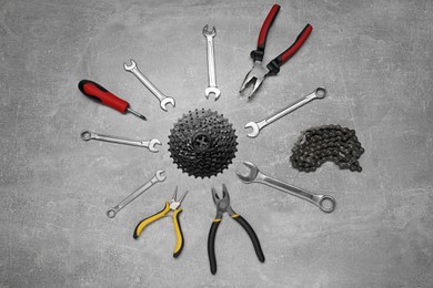 Wrenches, pliers, bicycle tire, cassette and chain on grey textured background, flat lay