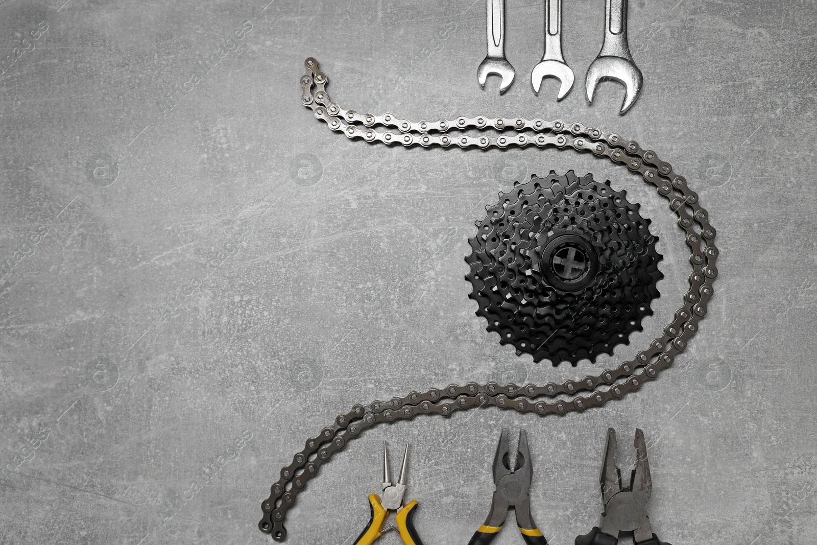 Photo of Wrenches, pliers, bicycle cassette and chain on grey textured background, flat lay. Space for text