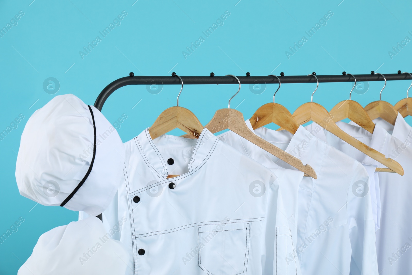 Photo of Different chef's uniforms on clothing rack against light blue background, closeup