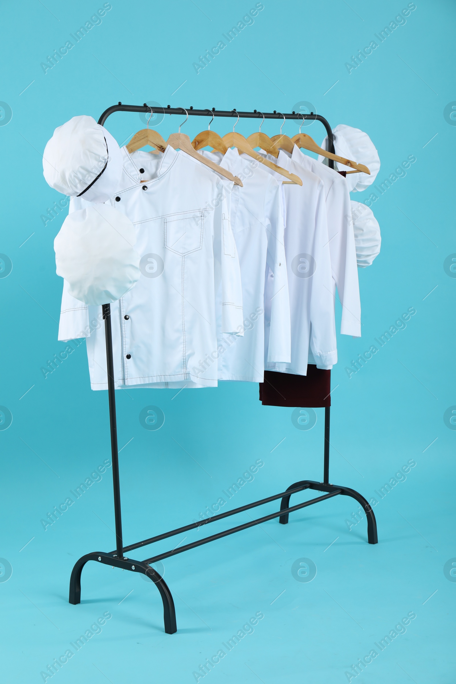 Photo of Different chef's uniforms on clothing rack against light blue background