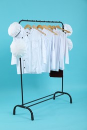 Different chef's uniforms on clothing rack against light blue background