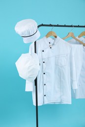 Different chef's uniforms on clothing rack against light blue background