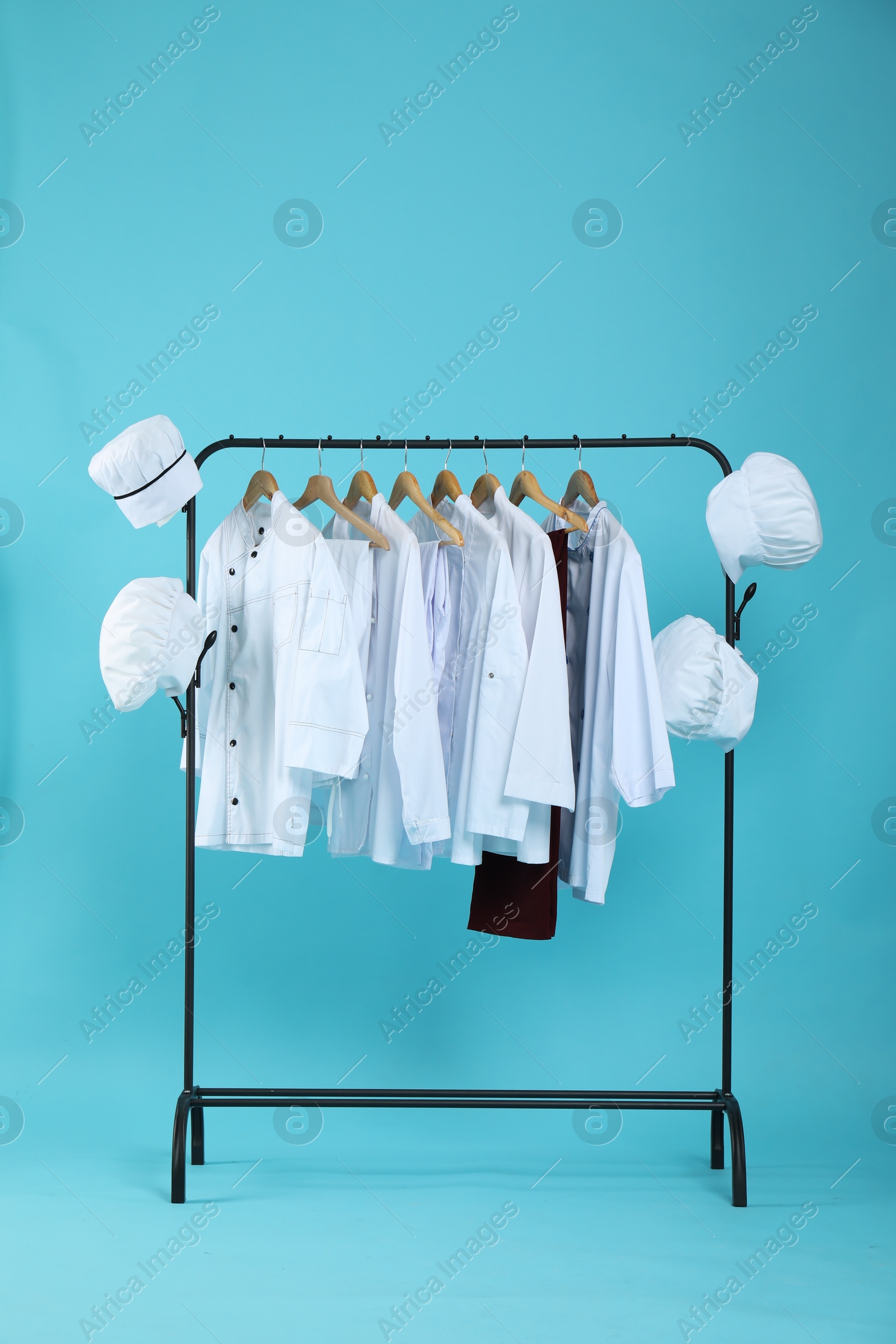 Photo of Different chef's uniforms on clothing rack against light blue background