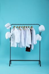 Different chef's uniforms on clothing rack against light blue background