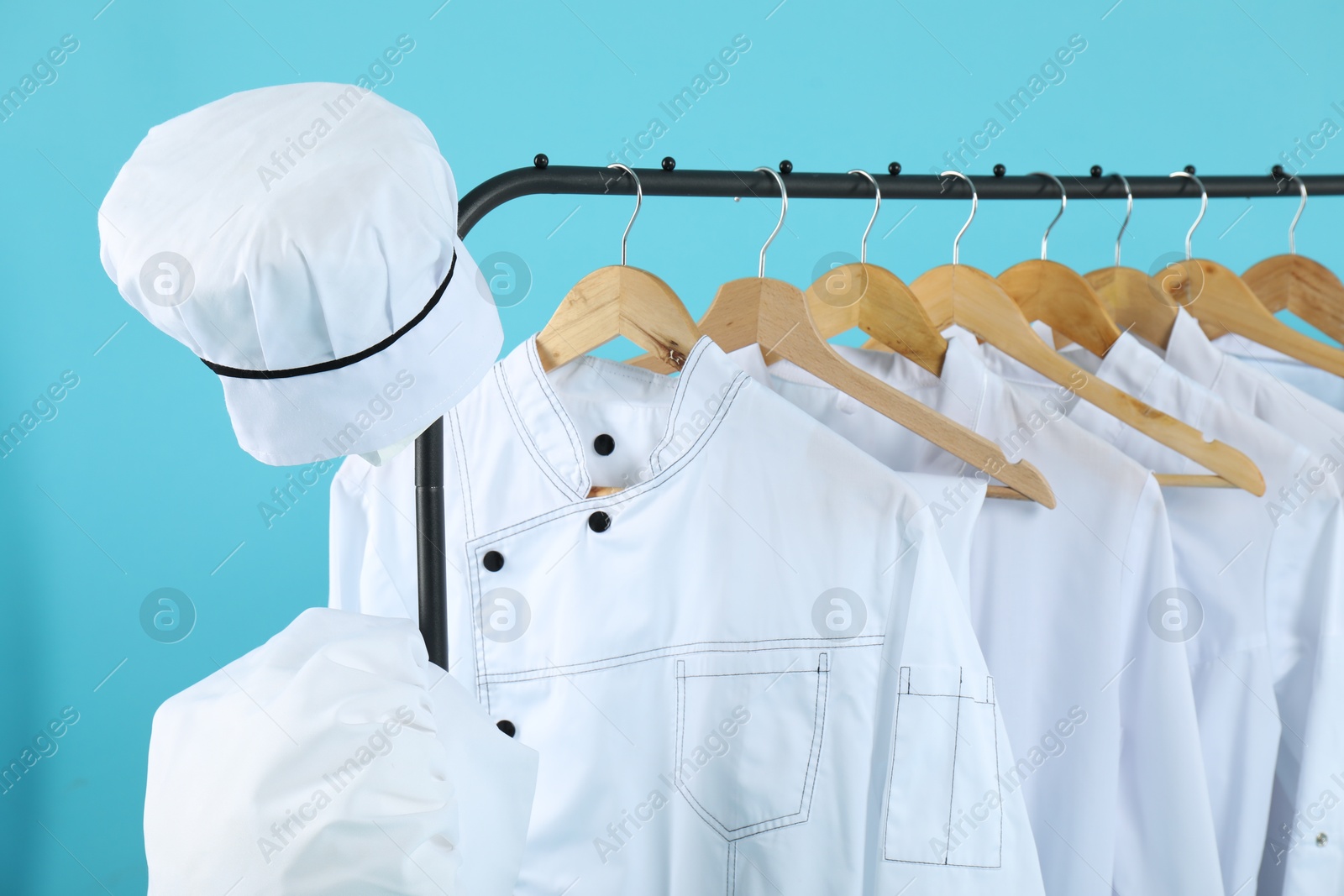 Photo of Different chef's uniforms on clothing rack against light blue background, closeup