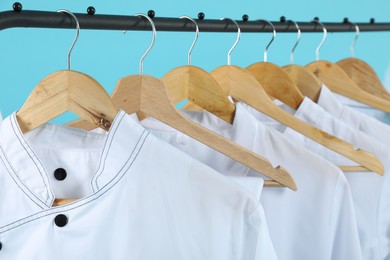 Different chef's coats on clothing rack against light blue background, closeup