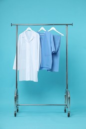 Photo of Different medical workers' uniforms on clothing rack against light blue background