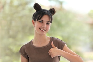 Portrait of smiling teenage girl showing thumbs up on blurred background