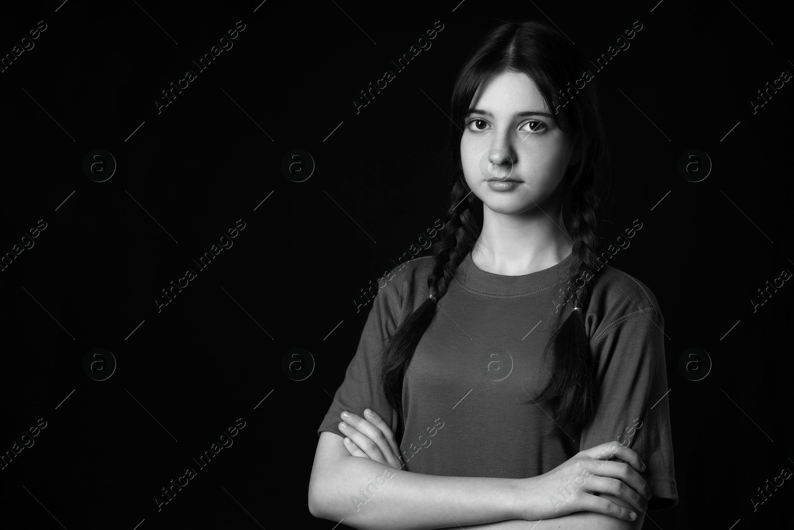 Photo of Portrait of teenage girl with crossed arms on dark background, space for text. Black and white effect