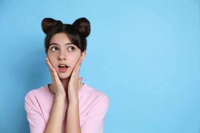 Photo of Portrait of surprised teenage girl on light blue background. Space for text