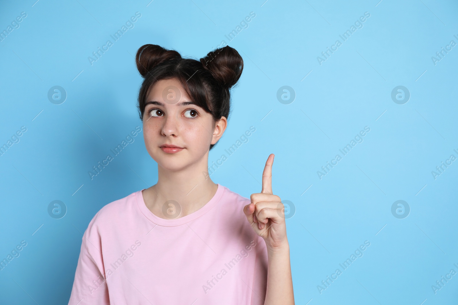 Photo of Portrait of cute teenage girl pointing at something on light blue background. Space for text