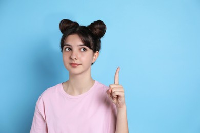 Portrait of cute teenage girl pointing at something on light blue background. Space for text