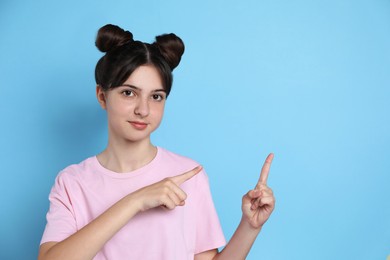 Photo of Portrait of cute teenage girl pointing at something on light blue background. Space for text