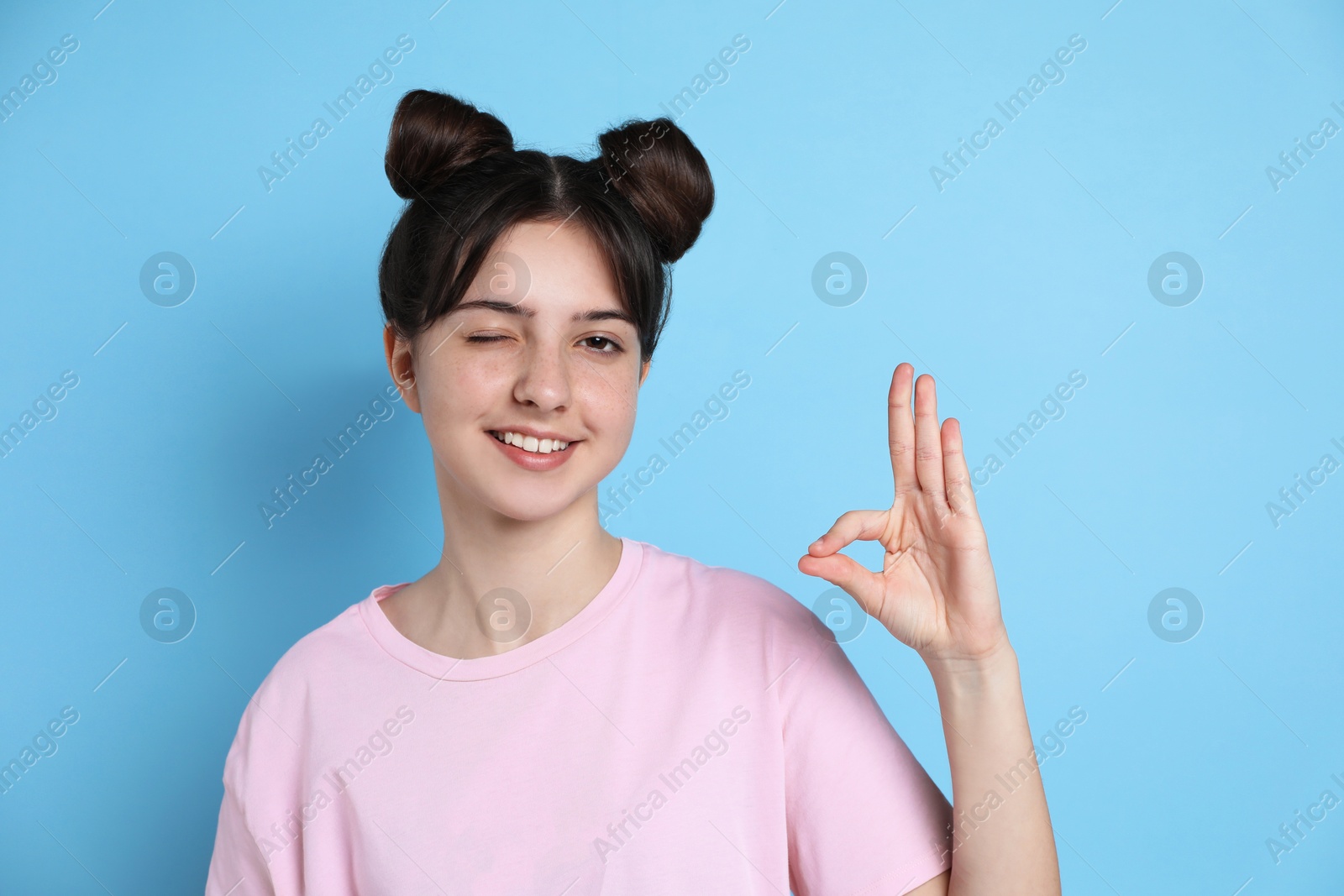 Photo of Portrait of smiling teenage girl showing ok gesture on light blue background