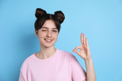 Portrait of smiling teenage girl showing ok gesture on light blue background