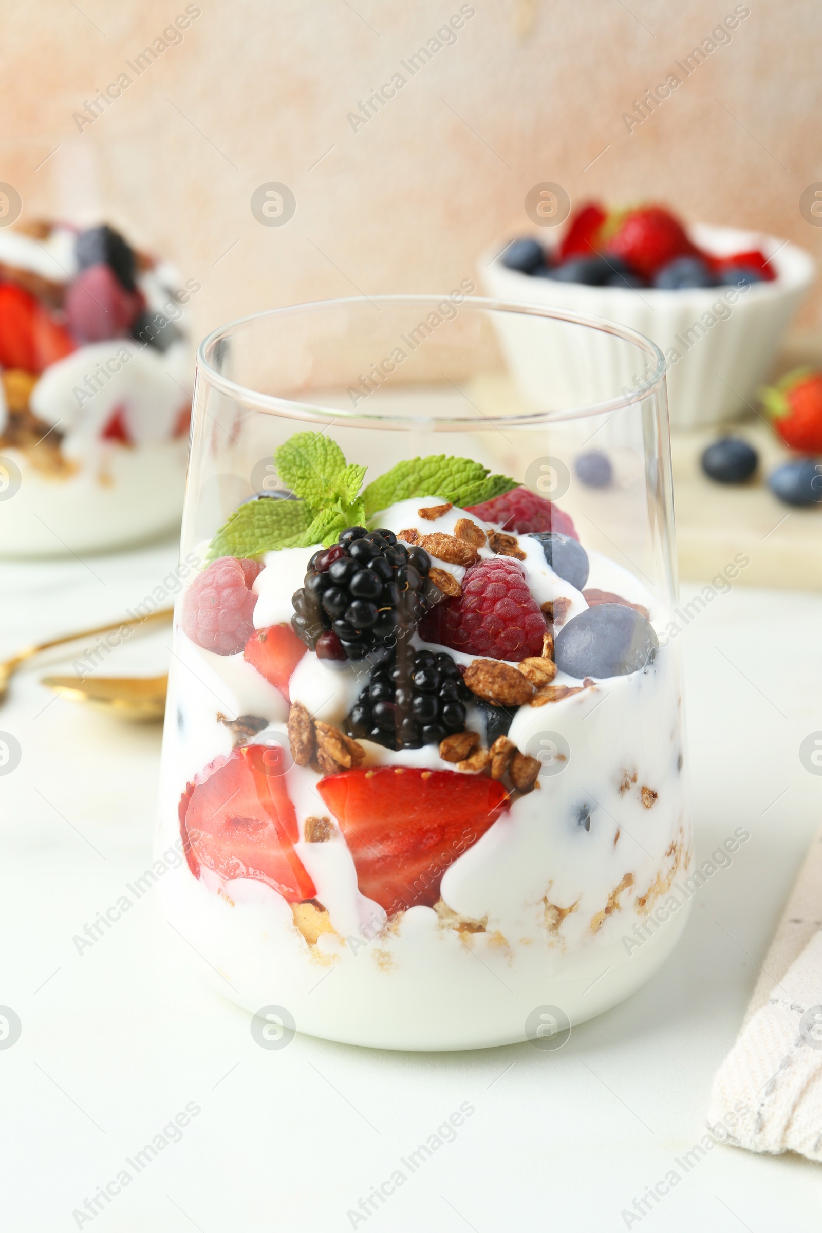 Photo of Tasty yogurt with fresh berries, granola and mint in glass on white table