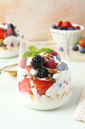 Photo of Tasty yogurt with fresh berries, granola and mint in glass on white table