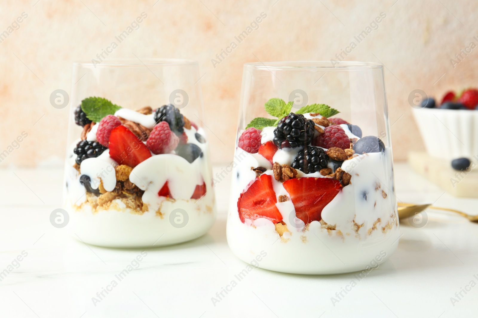 Photo of Tasty yogurt with fresh berries, granola and mint in glasses on white marble table