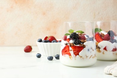 Tasty yogurt with fresh berries, granola and mint in glasses on white marble table, space for text