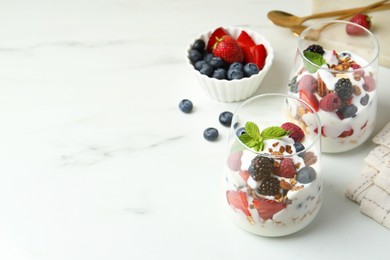 Photo of Tasty yogurt with fresh berries, granola and mint in glasses on white marble table, space for text