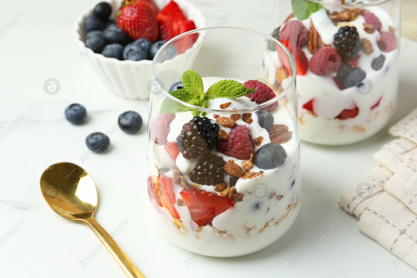 Photo of Tasty yogurt with fresh berries, granola and mint in glasses served on white table, closeup