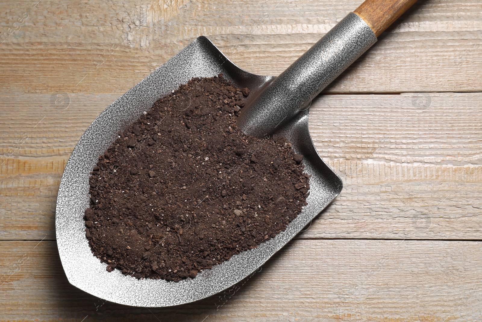 Photo of Metal shovel with soil on wooden table, top view