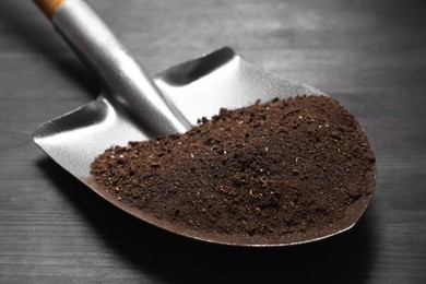 Photo of Metal shovel with soil on black wooden table, closeup