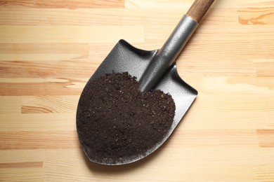 Metal shovel with soil on light wooden table, top view